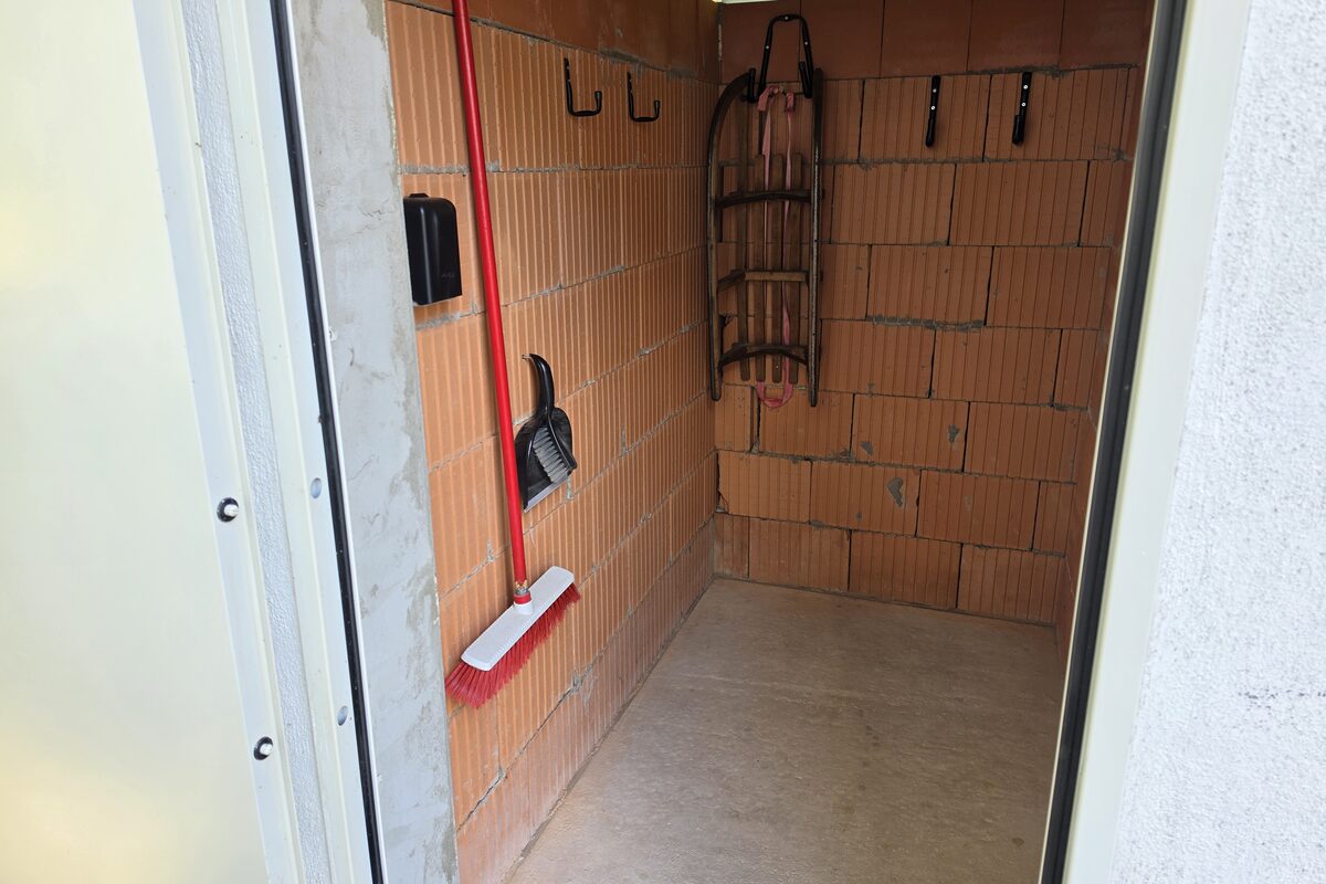 Geöffnete abschließbare Garage der Ferienwohnung in Winterberg, an der Wand hängen ein Holzschlitten für Gäste und Haken für Ausrüstung