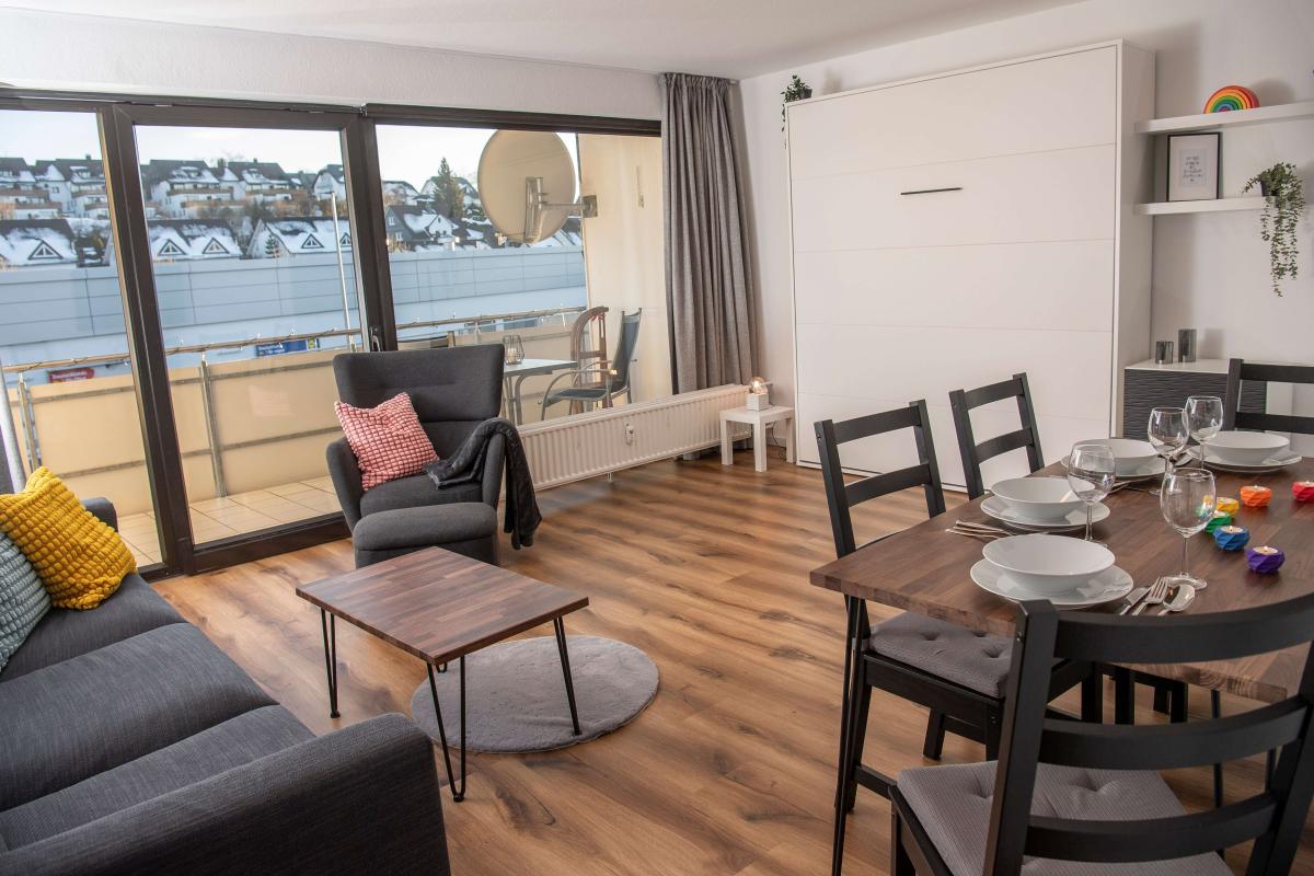 Wohnbereich der Ferienwohnung in Winterberg mit gedecktem Esstisch, Sofa und Balkontür