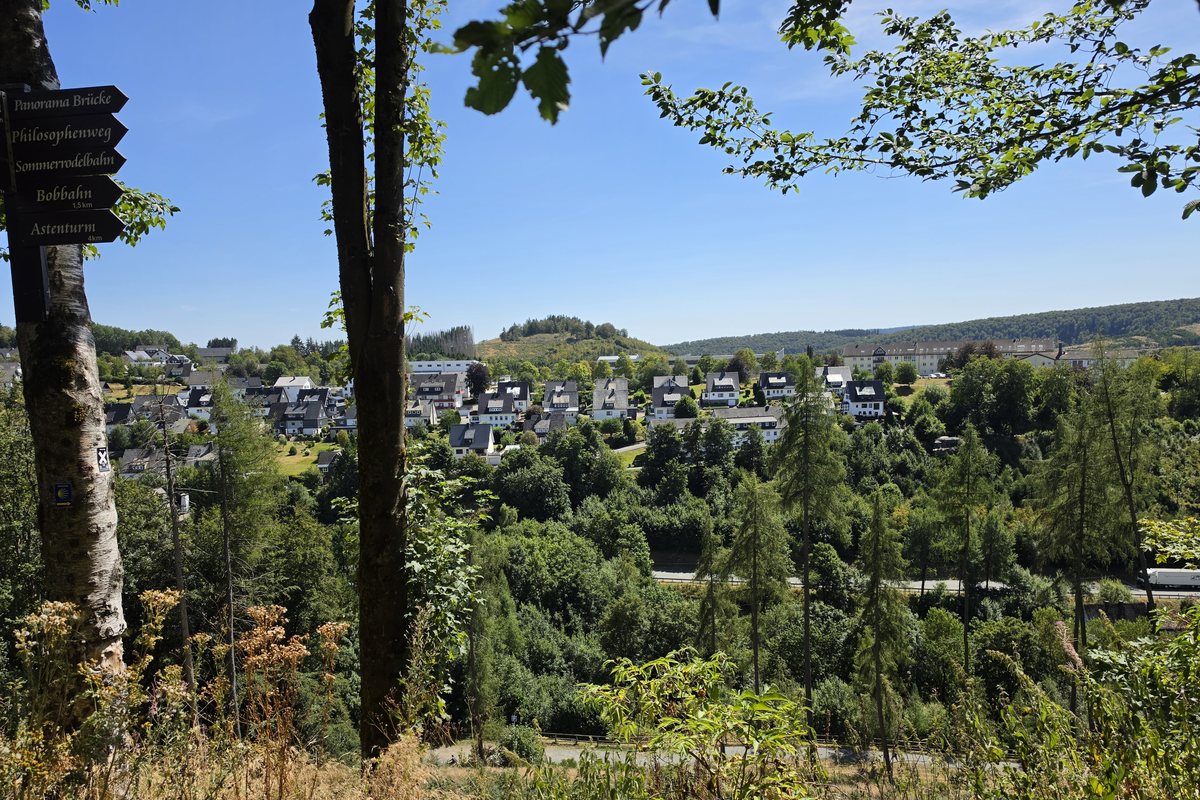 Wegweiser am Waltenberg in Winterberg mit den Zielen Panorama Brücke, Philosophenweg, Sommerrodelbahn, Bobbahn 1,5 km und Astenturm 4 km, dahinter der Blick über den Ort