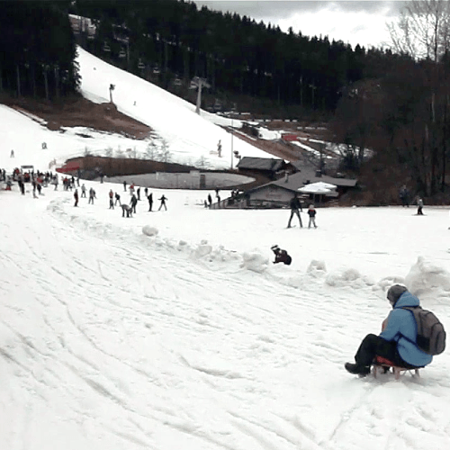 Winterlandschaft in Winterberg mit einem schneebedeckten Abhang, auf dem Menschen rodeln und Ski fahren